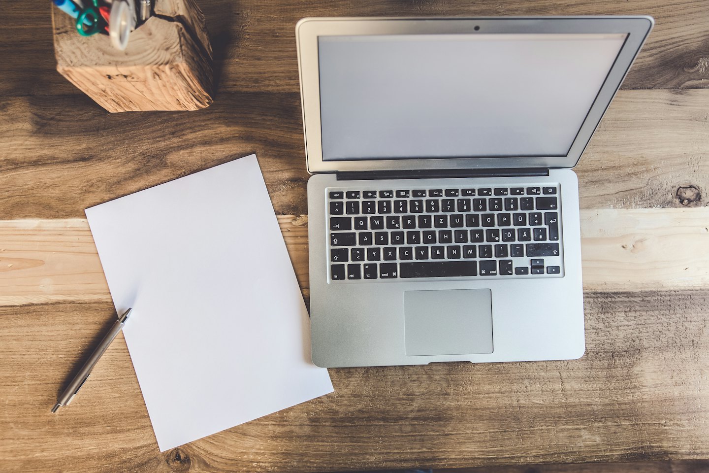 Computer portatile d'argento su una scrivania di legno con carta e penne.